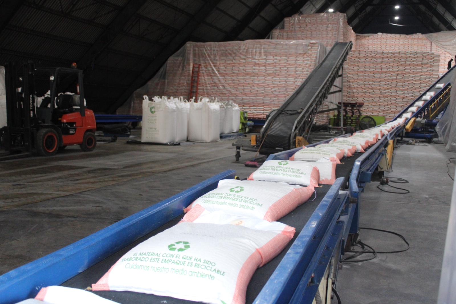 Sacos de azúcar empacada avanzando por una banda transportadora en la bodega de Ingenio La Cabaña